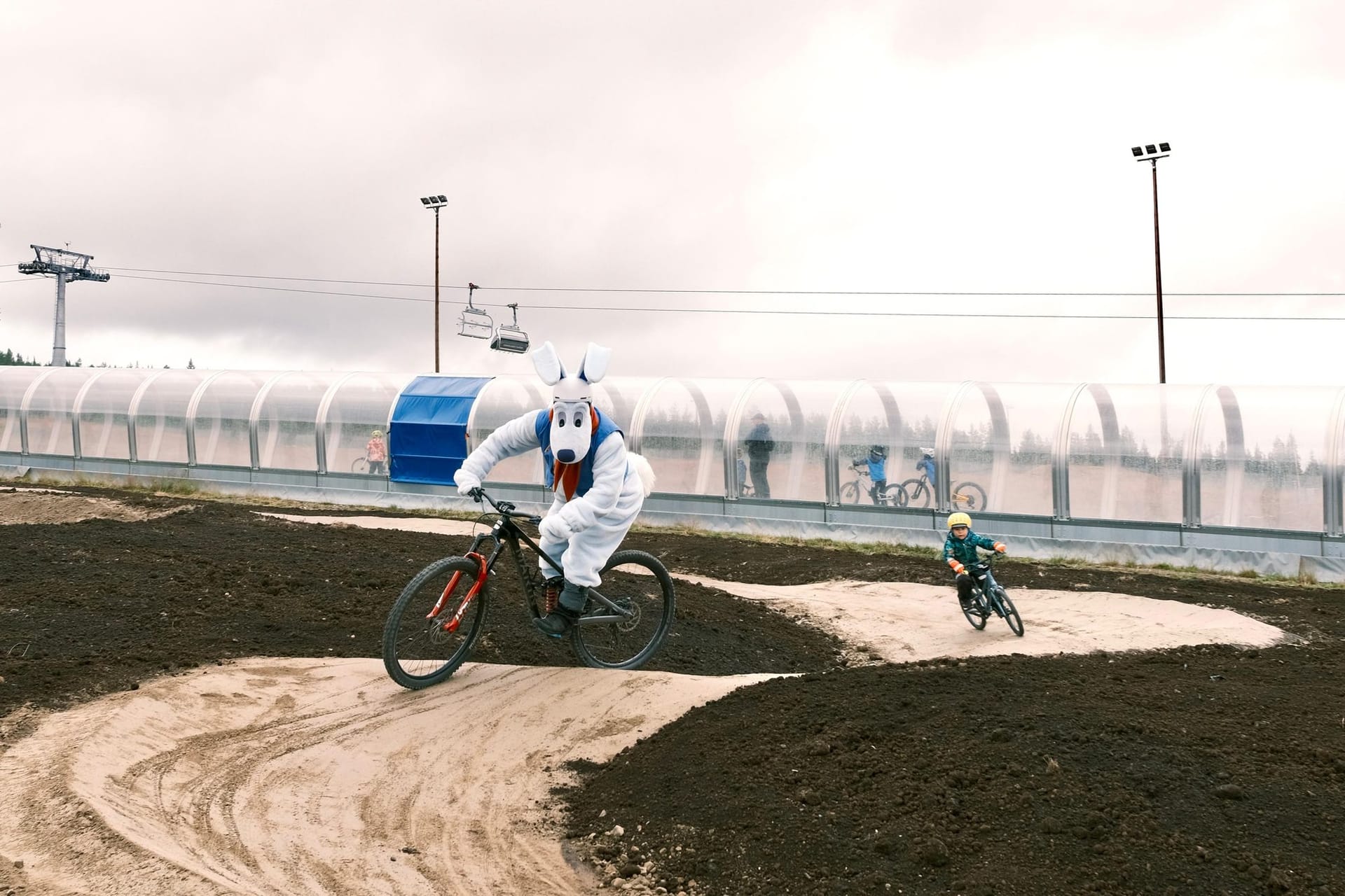 Mascot and a child riding in the Mini Bike Park beside the magic carpet at Ylläs